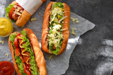 Çeşitli dolgulu sosisliler. Karanlık arka plan. yemek arkaplanı fotokopi alanı. Üst Manzara. Hardallı sosisli, ketçaplı, marullu, peynirli ve domatesli..