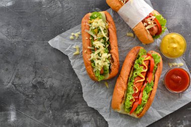 Çeşitli dolgulu sosisliler. Karanlık arka plan. yemek arkaplanı fotokopi alanı. Üst Manzara. Hardallı, ketçaplı, marullu, peynirli ve domatesli sosisli sandviç. Yakın çekim.