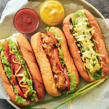 Farklı dolgulu üç sosisli sandviç. Yukarıdan bak. Hardallı, ketçaplı, marullu, peynirli ve domatesli sosisli sandviç. Yakın plan.