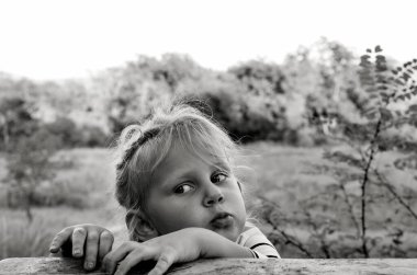 Yakışıklı beyaz bir bebeğin siyah beyaz portresini kapat. Çocukların samimi duyguları. Çocukluk anları. Köyün doğasında, tahta bir masanın yanındaki kız..