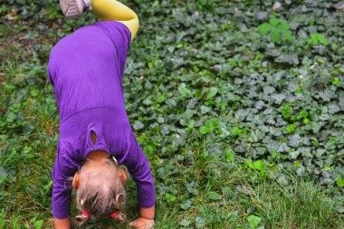 Yeşil yapraklı bir arka planda güzel bir çocuğun portresi. Çocuk baş aşağı duruyor. Bebek başının üstünde duruyor..