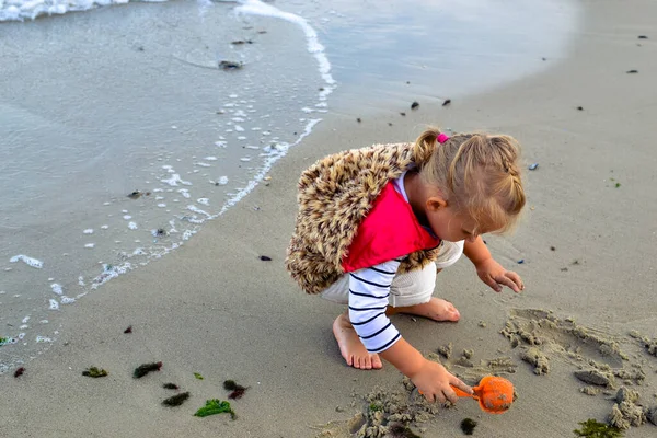 A gyermek játszik a vízzel és homokkal a naplementében. Egy őszi estén egy mezítlábas gyerek sétál a töltésen.. — Stock Fotó
