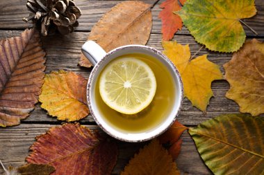 Tahta arka planda sıcak bir fincan çay. Sonbahar günü çay ve limonlu beyaz bardak. Sonbahar renkli yapraklar. Samimi bir konsept. Üst görünüm.
