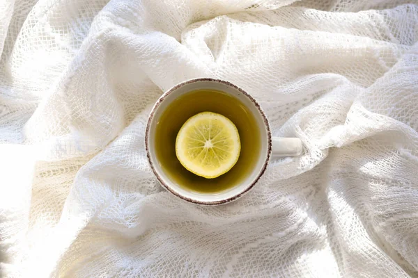 A cup with tea and lemon. Top view. White background. A cup on a white bed, sunbeams.