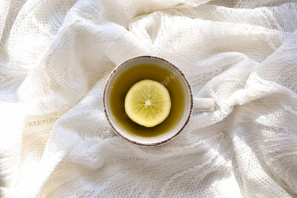 A cup with tea and lemon. Top view. White background. A cup on a white bed, sunbeams.