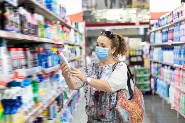 Older woman looking at a product inside the supermarket. She is wearing a medical mask.