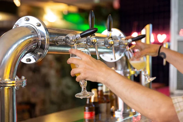 Close up of person\'s hands filling two beer mugs at once in a bar. Selective focus.