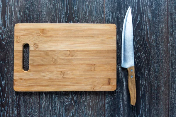 Tabla de cortar de madera y un liyng cuchillo sobre un fondo oscuro. Vista superior. Copiar espacio para texto —  Fotos de Stock