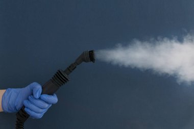 Mavi eldivenli kadın eli mavi arka planda ev buhar jeneratörlü hortum. Uzayı metin için kopyala. Alerji, virüs ve tozdan kaynaklanan dezenfeksiyon.