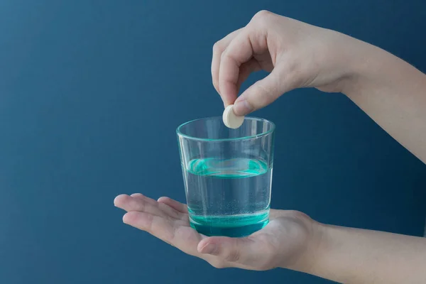 female hand drops an effervescent tablet into a transparent glass with water on a blue background. Copyspace for text. Recovery concept.