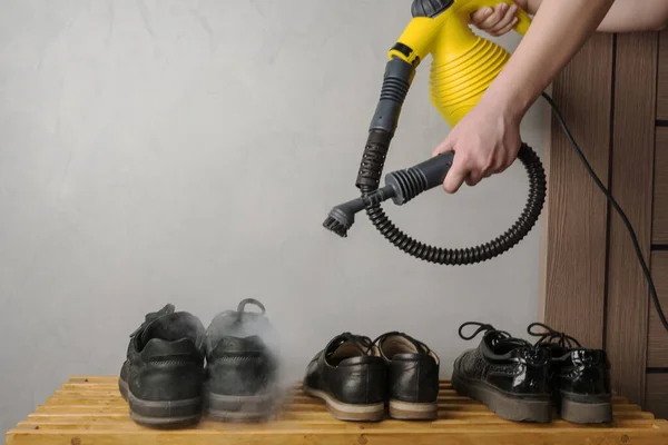 Kadın eli, siyah ayakkabıları buharla temizlemek için sarı buhar jeneratörünü tutuyor. Tozdan, topraktan, virüsten, kalıptan dezenfekte olmuş. Sağlık ve temizlik konsepti.