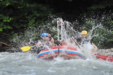 Team of people in raft in the middle of  mountain river. Splashing water from under the oars. Extreeme adventure and exiting experience. clipart