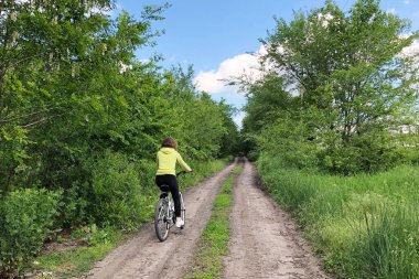 Kırsal yeşil yolda bisiklet süren genç bir bayan. Yaz tarlasında spor macerası. Sağlıklı yaşam tarzı kavramı.