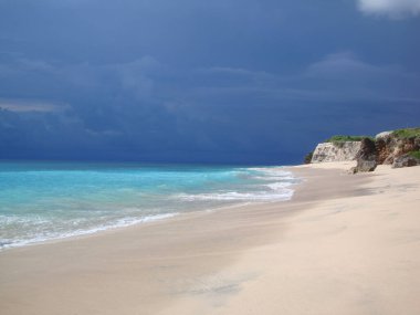 Turkuaz denizi ve karanlık dramatik gökyüzü, beyaz kumlu ve büyük kayalıklı kıyı şeridi, nefes kesen manzara, metin için kopyalanan boşluk. Seyahat için çarpıcı yerler..                               