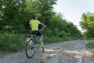 Çocuk yeşil ormandaki şehir yolunda büyük bir bisiklete biniyor. Mutlu çocukluk ve yaz tatili konsepti. Metin için polis alanı.