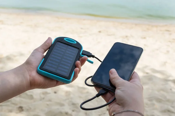 Kadın elleri bir elinde güneş enerjisi, diğer elinde siyah akıllı telefon tutuyor. Dışarıda elektrik olmadan şarj etmeye çalışıyorum. Her durumda zor durumda kalabilme yeteneği.
