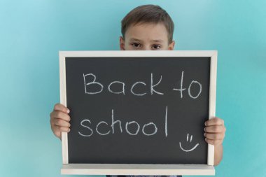 Okullu çocuk tahtanın arkasında duruyor ve okula tebeşirle yazılmış bir yazıyla geri dönüyor. Metin için alanı kopyala. 