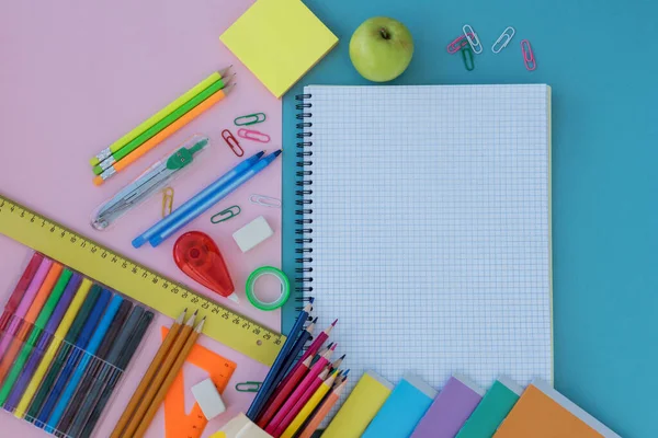 Okul malzemelerinin üst görüntüsü ve yeşil elma mavi ve pembe arka planda yatıyor. Boşluğu beyaz defterde metin için kopyala. Okul konseptine dönelim.. 