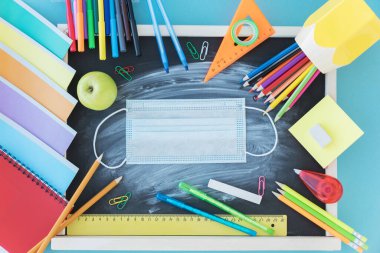 Okul malzemelerinin en üst görüntüsü tahtada ve sağlık maskesinde yer alıyor. Okul konseptine geri dönelim. Coronavirus salgınından sonra yeni gerçeklik ve okul için kısıtlamalar.