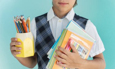 Okul üniformalı çocuğun yakın plan görüntüsünde bir yığın defter, elma, kalem ve kurşun kalemli sarı bardak var. Okul konseptine dönelim..