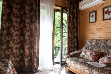 Rusya, GELENDGIK - 4 Ağustos 2020. Balkon kapısı açık, perdeleri de açık olan rahat bir oda. Odanın dışında aydınlık bir yaz günü, evin dışında yeşil park. Rahatlatıcı iç mekan. 