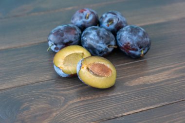 Birkaç olgun eriğin görüntüsü koyu ahşap arka planda yatar, bir erik yarıya bölünür. Uzayı metin için kopyala. Sağlıklı vitamin yiyeceği konsepti