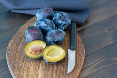 Olgun koyu erikler kahverengi ahşap kesme tahtasının üzerinde yatar, yanında bir bıçak vardır ve olgun bir erik ikiye ayrılır. Tahta arka planda. sağlıklı beslenme konsepti. Hasat zamanı.