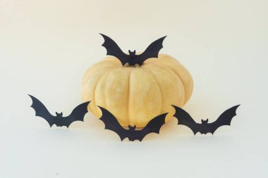 Açık arkaplanda sarı bir balkabağının yanında uçan siyah yarasaların dört silueti. Uzayı metin için kopyala. Cadılar Bayramı konsepti. Kartpostal düzeni.