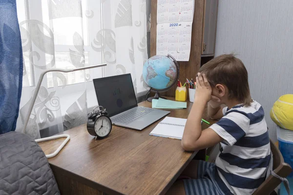 schoolboy sits at desk, looks into  laptop screen and thinks about challenging school tasks.  Home distant education concept. Difficulties of studing withou teacher.