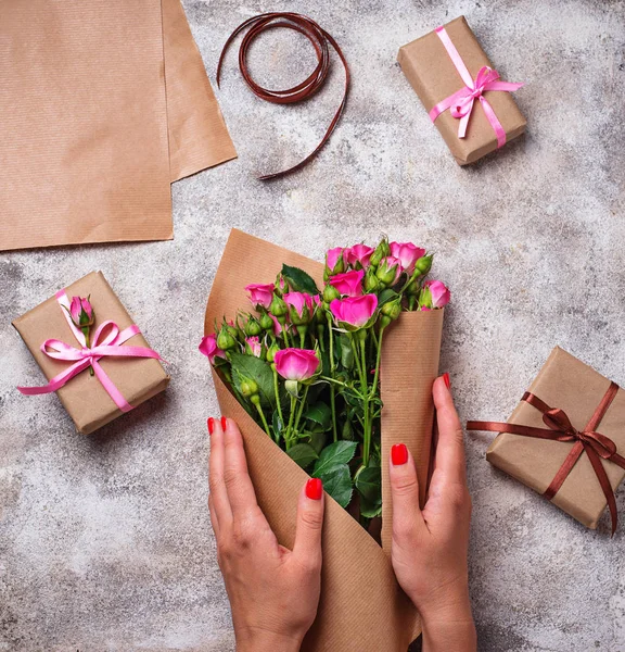 Womens hands wrap a bouquet of roses in paper