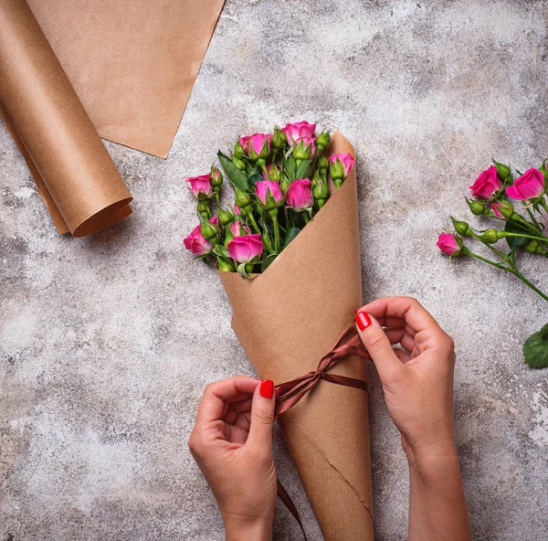 Womens hands wrap a bouquet of roses in paper