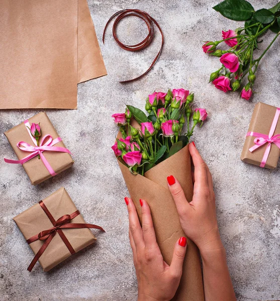 Womens hands wrap a bouquet of roses in craft paper. Top view