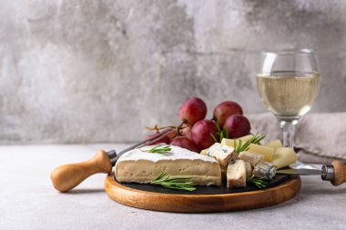 Bir bardak şarap, değişik türde yumuşak peynir ve üzümler.