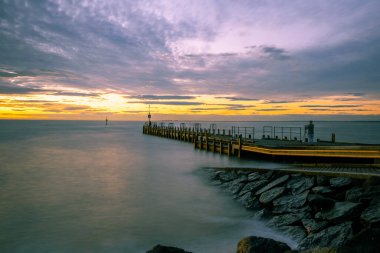 Gün batımında fotoğrafçı silueti ve tripodla ipeksi, pürüzsüz okyanus suyu ve rıhtımın uzun pozu.