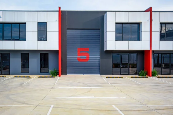 Industrial building with empty parking lot. Closed warehouse door with large number 5 painted on it.