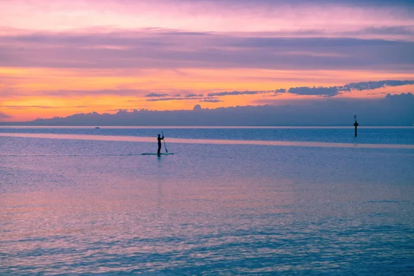 日没時に海のパドルボードに立つ人のシルエット — ストック写真