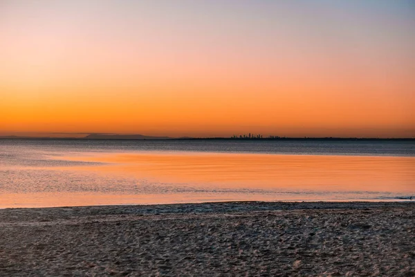 海のビーチの上の日没時の距離で遠くの都市の高層ビル コピースペースとミニマリストの風景 — ストック写真