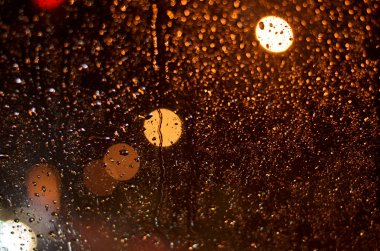 Bir pencere camı geceleri sokak lambaları yaktı bir araba üzerinde yağmur damlaları.