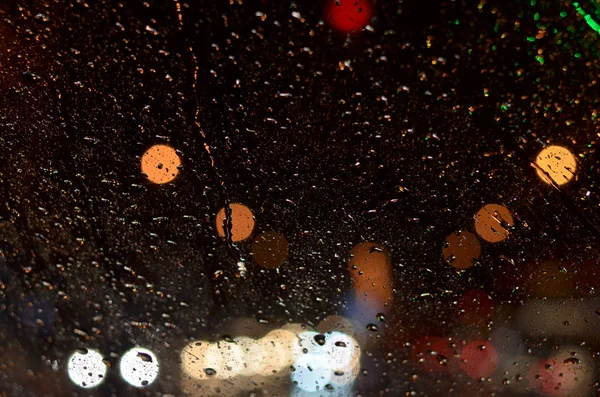 Капли дождя на оконном стекле машины, освещенной уличными фонарями ночью . — стоковое фото
