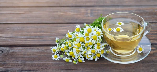 Té de manzanilla fragante en una taza de vidrio y un ramo de flores — Foto de Stock