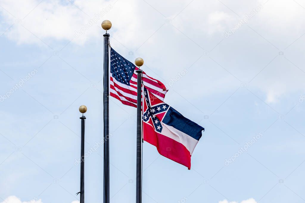 Flag poles with United States of America flag and State of Mississippi Flag waving in the wind against blue sky.