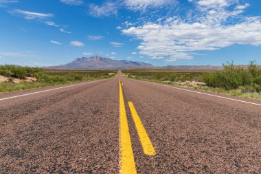 Çölde uzun düz bir yol, bulutlu mavi gökyüzünün altında güzel bir dağ sırasına çıkıyor.