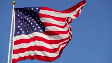 Rüzgarda dalgalanan parlak Amerikan bayrağı, yavaş çekimde, güneş tarafından aydınlatılan canlı kırmızı beyaz ve mavi renklerle, mavi gökyüzüne karşı,.