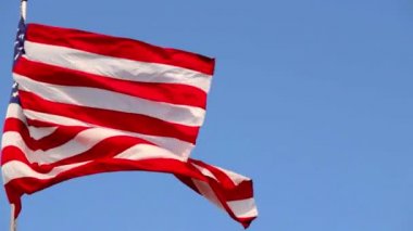 Mavi gökyüzüne karşı rüzgarda dalgalanan canlı Amerikan bayrağı.