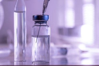 Ampul, cam şişeler ve mavi zemin üzerinde koronavirüs aşısı olan tıbbi bir şırınga.