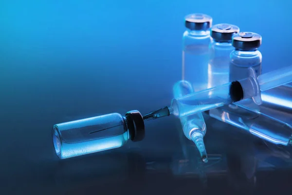 ampoule, glass vials and a medical syringe with a coronavirus vaccine on a blue background