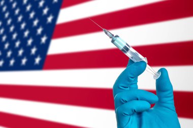 ABD 'de Coronavirus salgınına karşı savaşın. ABD bayrağının arka planında COVID-19' un tedavisi için aşı ile doktor eli eldiveni. ABD 'de grip aşısı