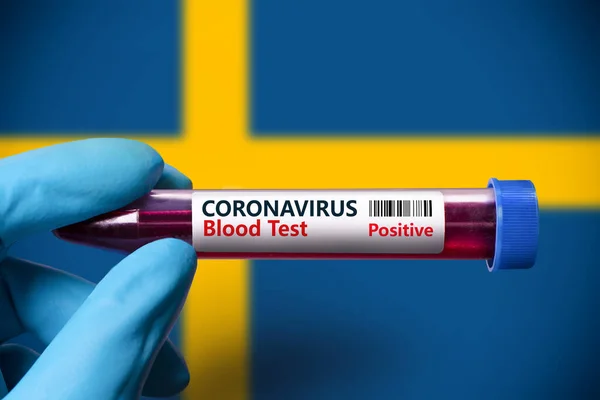 A test tube with a positive test for coronavirus against the background of the flag of Sweden . COVID-19 concept for fighting the coronavirus epidemic in Sweden