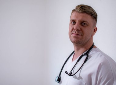 Gülümseyen beyaz erkek doktor portresi beyaz tıbbi üniforma, steteskop giyer.