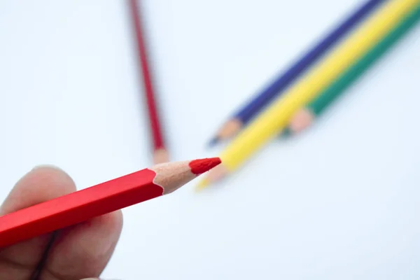 A person holding a red color wood pencil crayon with a very blurry background with pencils